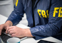 FBI RAIDS Election Hub — Ballots SEIZED! Person in FBI jacket working on laptop.