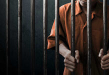 Man in orange prison uniform behind jail bars.