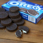 A pile of Oreo cookies next to an open package on a wooden surface
