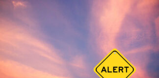 Yellow alert sign against a colorful sunset sky