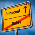 A yellow road sign displaying 'Innocent' pointing up and 'Guilty' crossed out
