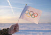 Olympian Hospitalized After Breaking Neck Hand holding Olympic flag in snowy landscape