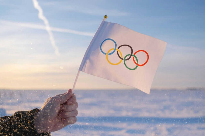 shutterstock_2097149272.jpg Hand holding Olympic flag in snowy landscape