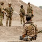 Military personnel in tactical gear discussing in a desert-like environment