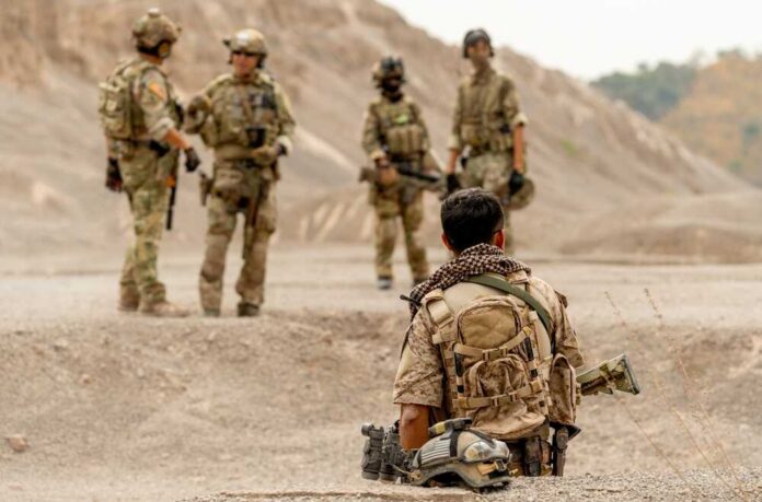 Military personnel in tactical gear discussing in a desert-like environment