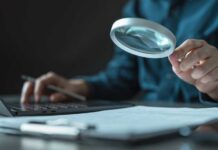 Person using a magnifying glass while working on a laptop
