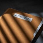 A brown folder with the name 'EPSTEIN' on it, partially illuminated by light and casting shadows