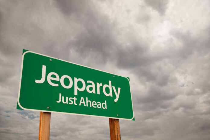 Green road sign indicating 'Jeopardy' ahead with a cloudy sky