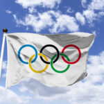 Olympic flag waving against a blue sky with clouds