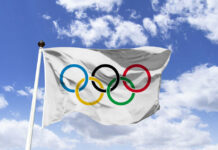 Olympic flag waving against a blue sky with clouds