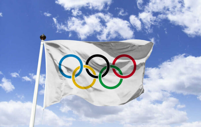 shutterstock_1404831047.jpg Olympic flag waving against a blue sky with clouds