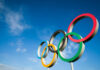 Five colorful Olympic rings against a clear blue sky