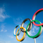 Five colorful Olympic rings against a clear blue sky