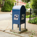 Blue USPS mailbox on a residential street corner.