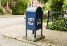 Blue USPS mailbox on a residential street corner.