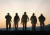 Five armed soldiers silhouetted against sunset background.