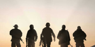 Five armed soldiers silhouetted against sunset background.