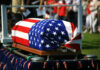 American flag draped over a casket at ceremony.