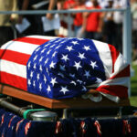 American flag draped over a casket at ceremony.
