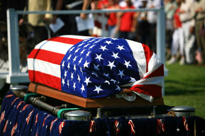 American flag draped over a casket at ceremony.