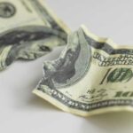 Torn and crumpled hundred dollar bills on a white surface