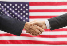 Two hands shaking in front of American flag
