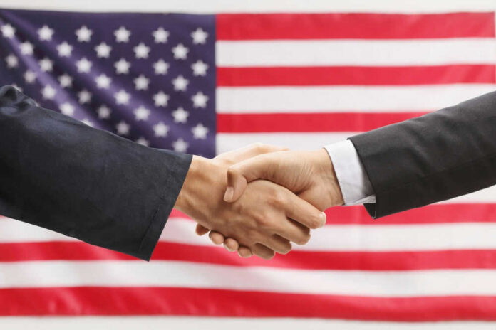 Two hands shaking in front of American flag