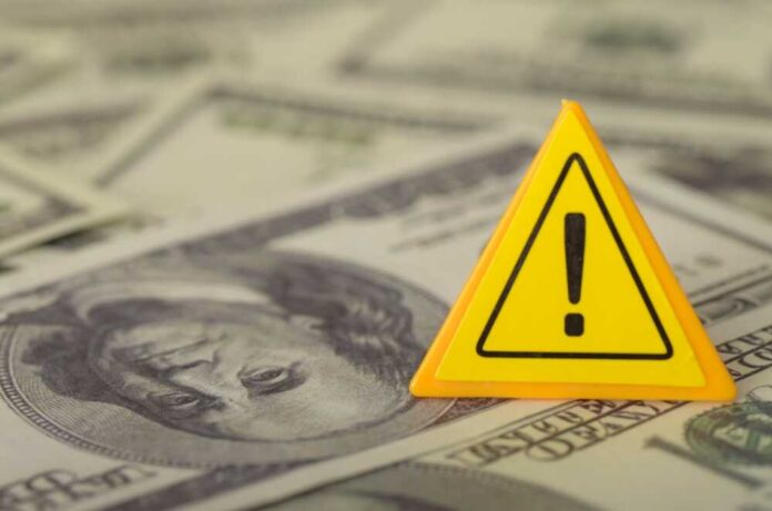 A yellow warning sign placed on a background of dollar bills