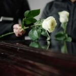 Two individuals placing white roses on a coffin during a funeral