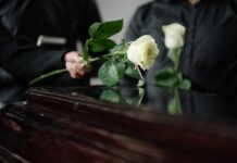 Two individuals placing white roses on a coffin during a funeral