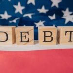 Wooden blocks spelling 'DEBT' on a background of the American flag