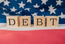 Wooden blocks spelling 'DEBT' on a background of the American flag