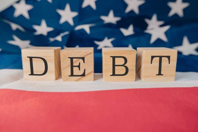 Wooden blocks spelling 'DEBT' on a background of the American flag