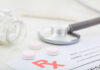 A stethoscope, prescription pad, and pink tablets on a table