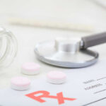 A stethoscope, prescription pad, and pink tablets on a table