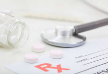 A stethoscope, prescription pad, and pink tablets on a table