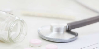 A stethoscope, prescription pad, and pink tablets on a table