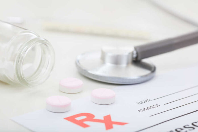 A stethoscope, prescription pad, and pink tablets on a table