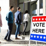 People entering building with Vote Here sign nearby.