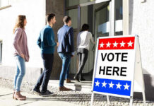 People entering building with Vote Here sign nearby.