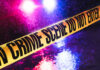 Crime scene tape with flashing lights in background.