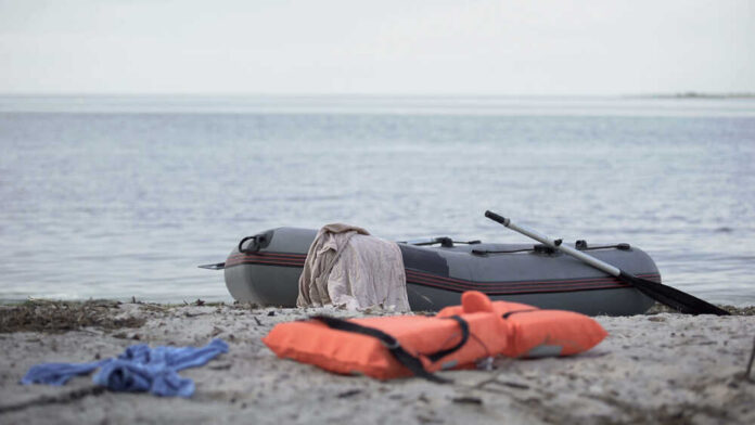 shutterstock_1539373601.jpg An inflatable boat on the beach with a life jacket and clothes nearby
