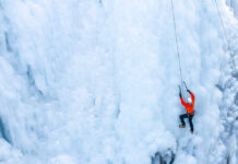 A climber in an orange jacket scaling a frozen ice wall