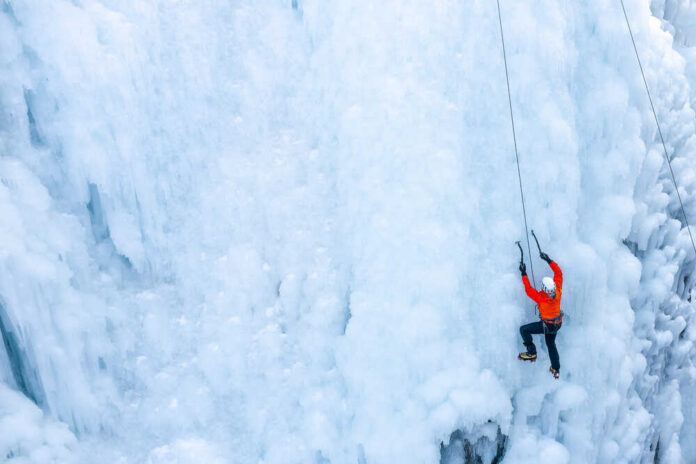 shutterstock_2001558071.jpg A climber in an orange jacket scaling a frozen ice wall