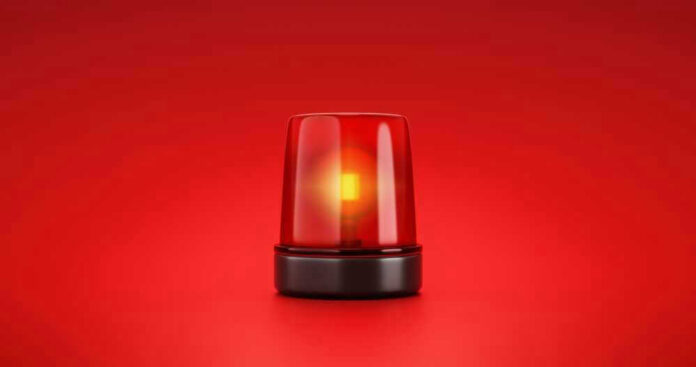 shutterstock_2053758056-1 Red emergency light on solid red background.