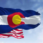 Colorado and United States flags waving against sky.