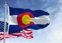 Colorado Governor Frees Election Denier Early Colorado and United States flags waving against sky.