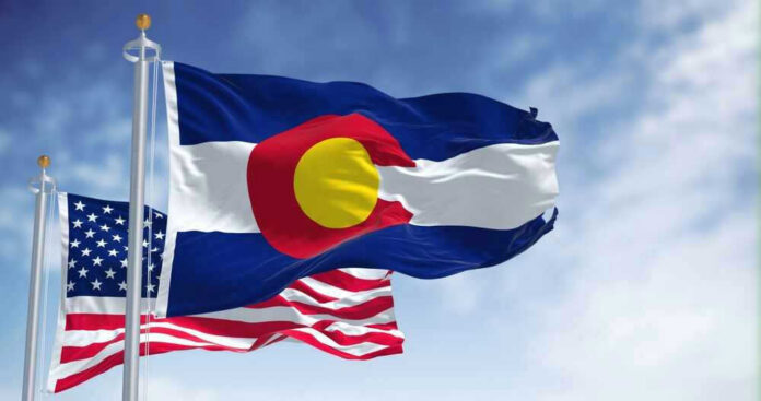 Colorado and United States flags waving against sky.