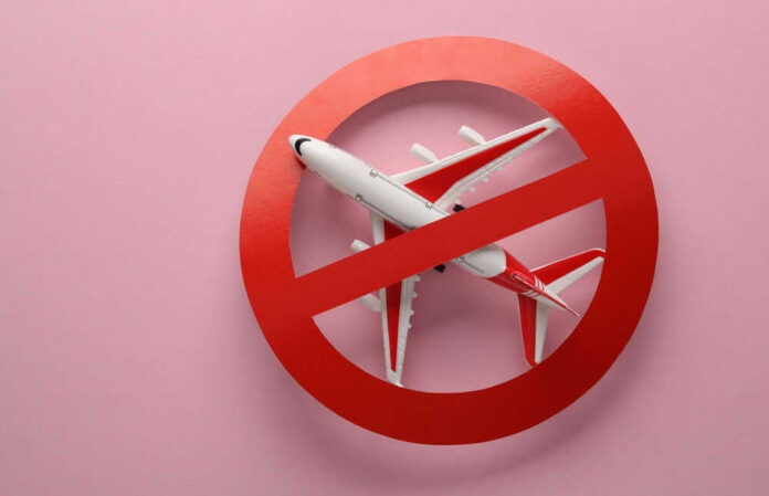 shutterstock_2273482921 Airplane inside red prohibition sign on pink background.