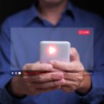 AI Voice Scam Stuns Mom – $5,400 Gone! Person holding a smartphone with a live streaming interface